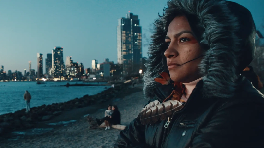Film still from YANUNI: Chief Juma Xipaia in a hooded coat along the New York City waterfront at dusk.